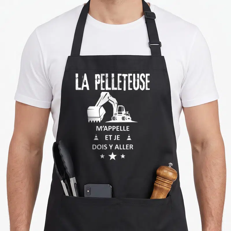 Tablier de cuisine noir avec illustration blanche d'une pelleteuse et texte humoristique sur fond uni.