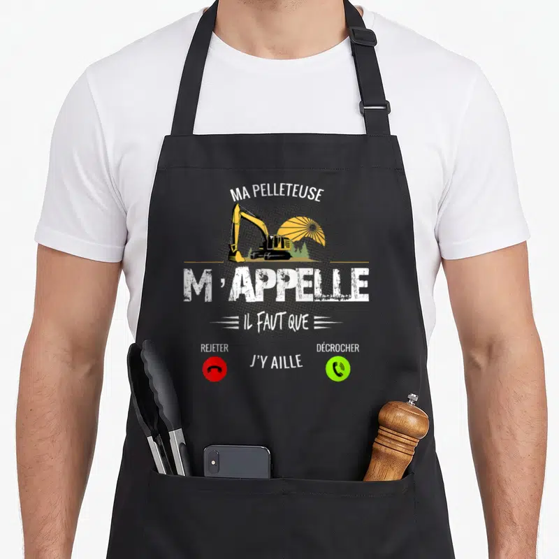 Tablier de cuisine noir avec illustration de pelle jaune et texte Ma Pelleteuse m'appelle sur fond gris uni.