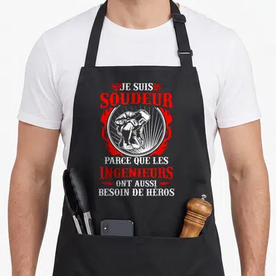 Tablier de cuisine noir avec illustration d'un soudeur et texte Je suis soudeur parce que les ingénieurs ont besoin de héros en rouge et blanc.
