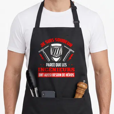 Tablier de cuisine noir avec casque de soudage, torches et texte Je suis soudeur ingénieurs ont besoin de héros.