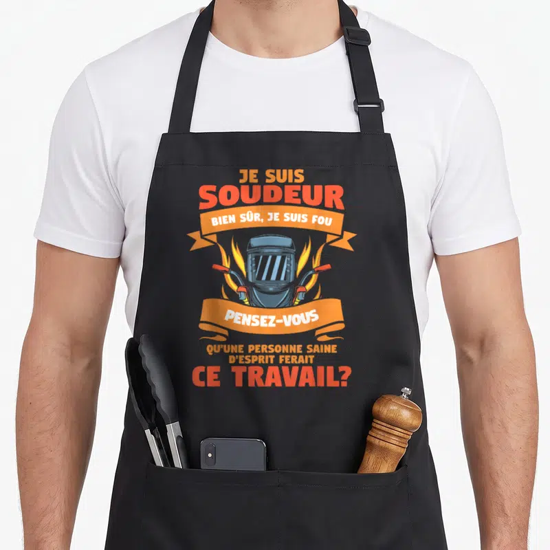 Tablier de cuisine noir avec illustration d'un casque de soudage, des flammes et un texte humoristique en orange et blanc.