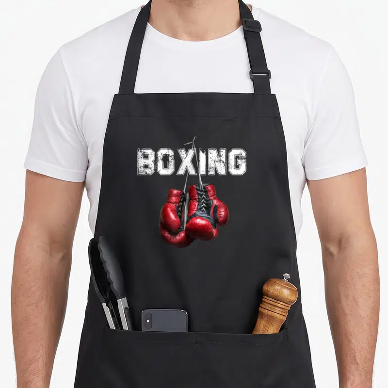 Tablier de cuisine noir avec l'inscription BOXING et une paire de gants de boxe rouges suspendus par les lacets.