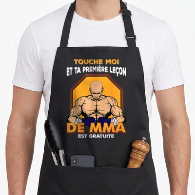 Tablier de cuisine noir avec illustration d'un combattant MMA musclé et texte humoristique sur fond orange octogonal.