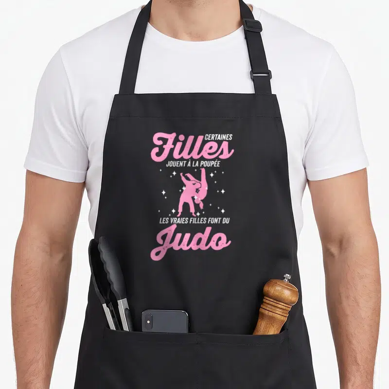Tablier de cuisine noir avec silhouette judoka rose et texte Certaines filles jouent à la poupée les vraies filles font du Judo.