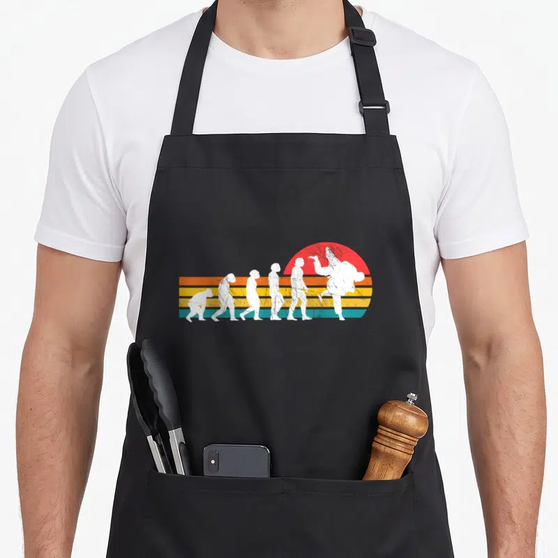 Tablier de cuisine noir avec illustration évolutive d'un homme transformé en judoka sur fond de soleil coloré.