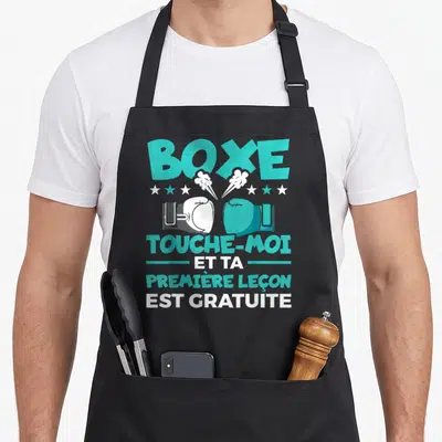 Tablier de cuisine noir avec gants de boxe turquoise et texte humoristique sur la première leçon gratuite.