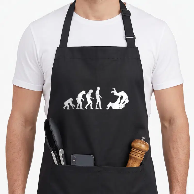 Tablier de cuisine noir avec silhouette blanche représentant l'évolution humaine vers le jiu-jitsu, style gravure distressed.