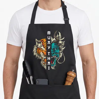 Tablier de cuisine noir avec illustration tigre orange et démon bleu turquoise, texte Muay Thai Thaï en blanc au centre.