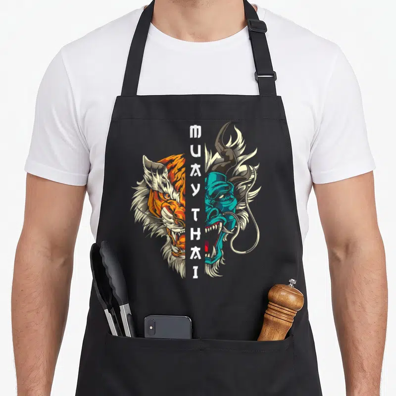 Tablier de cuisine noir avec illustration tigre orange et démon bleu turquoise, texte Muay Thai Thaï en blanc au centre.