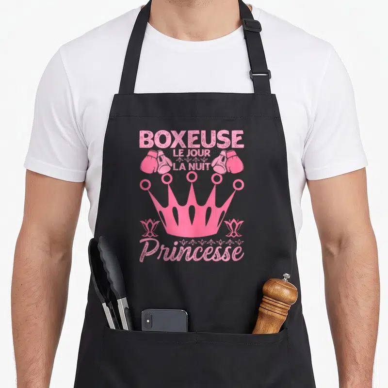 Tablier de cuisine noir avec inscription Boxeuse Le Jour La Nuit Princesse et illustration de gants roses surmontés d'une couronne.