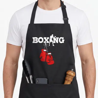 Tablier de cuisine noir avec inscription BOXING blanche et illustration de gants de boxe rouges suspendus par leurs lacets.