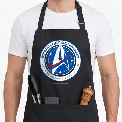 Tablier de cuisine noir avec le logo circulaire bleu et blanc de Starfleet Command et une étoile centrale rouge.