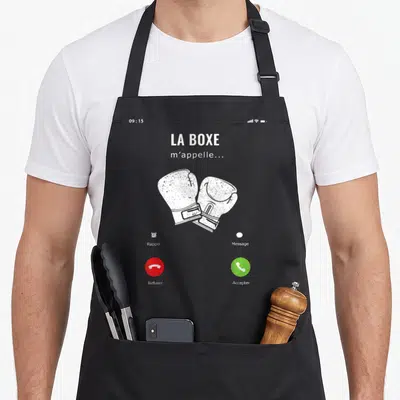 Tablier de cuisine noir avec interface d'appel téléphonique affichant La Boxe m'appelle et deux gants de boxe blancs croisés au centre.