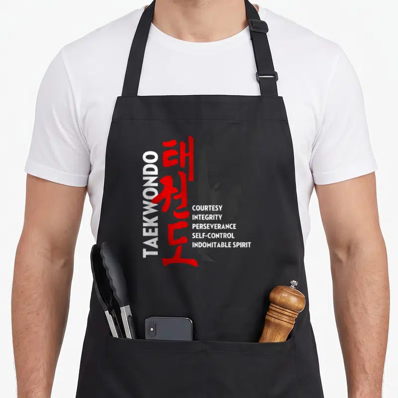 Tablier de cuisine noir avec silhouette de pratiquant de taekwondo et texte sur les principes de courtoisie et d'intégrité.