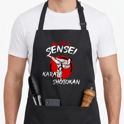 Tablier de cuisine noir avec illustration d'un karatéka effectuant un coup de pied devant un cercle rouge et le texte Meilleur Sensei Karate Shotokan.