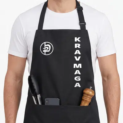 Tablier de cuisine noir avec logo circulaire blanc et texte Krav Maga disposé verticalement sur le côté droit.