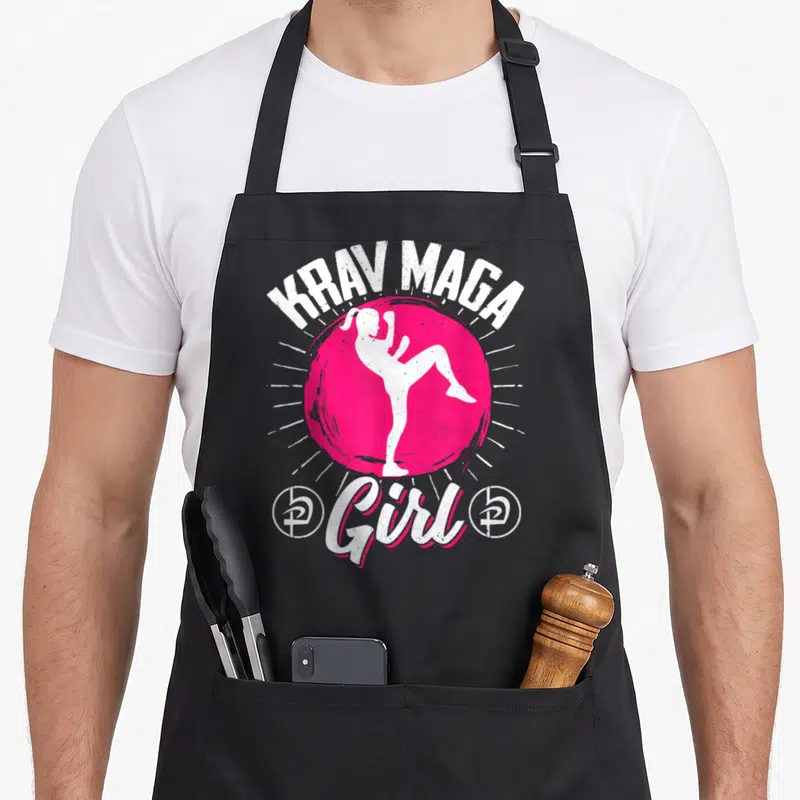 Tablier de cuisine noir avec silhouette blanche effectuant un coup de pied dans un cercle rose et le texte Krav Maga Girl.
