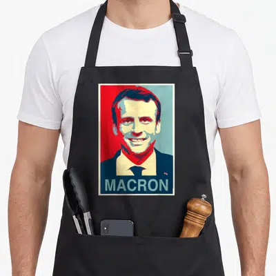 Tablier de cuisine noir avec un portrait stylisé de Macron en rouge et bleu et le texte MACRON en bas.