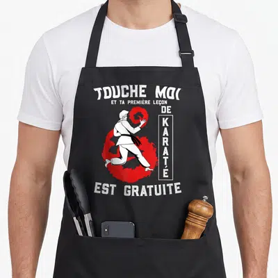Tablier de cuisine noir avec illustration d'un homme en kimono blanc effectuant un geste de karaté devant un cercle rouge stylisé.