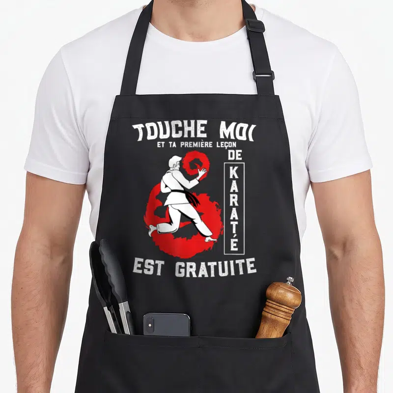 Tablier de cuisine noir avec illustration d'un homme en kimono blanc effectuant un geste de karaté devant un cercle rouge stylisé.