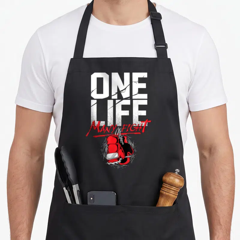 Tablier de cuisine noir avec gants de boxe rouges et texte One Life Many Fight en typographie blanche et rouge.