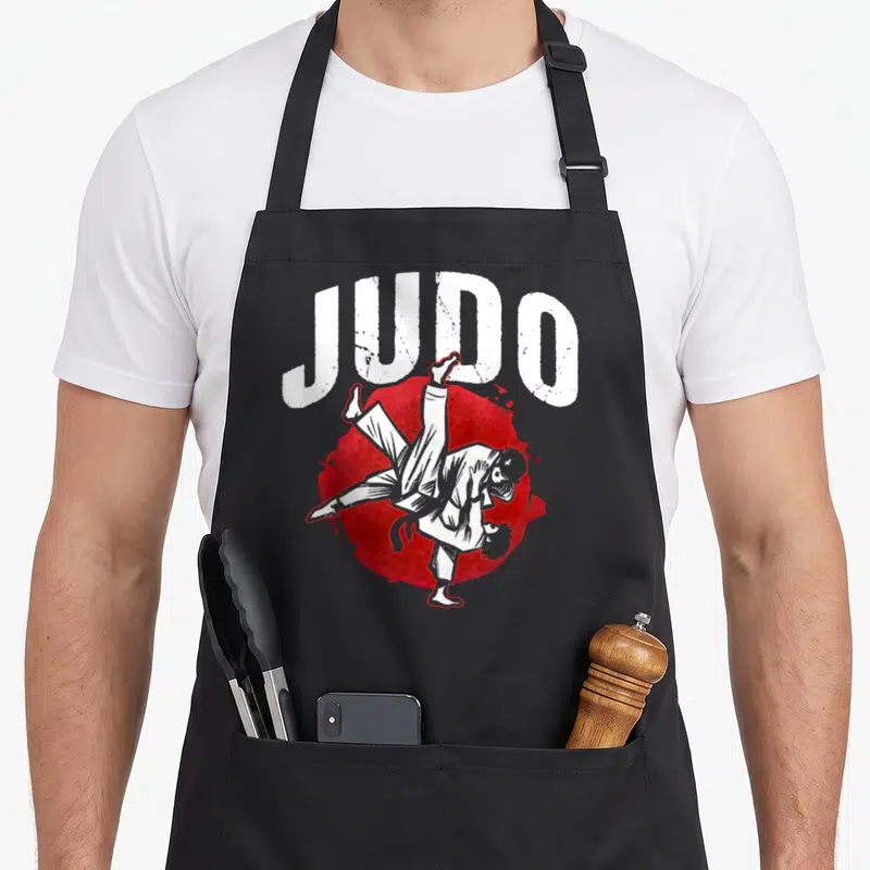 Tablier de cuisine noir avec illustration blanche d'un judoka projeté sur un cercle rouge et le texte JUDO en lettres capitales.
