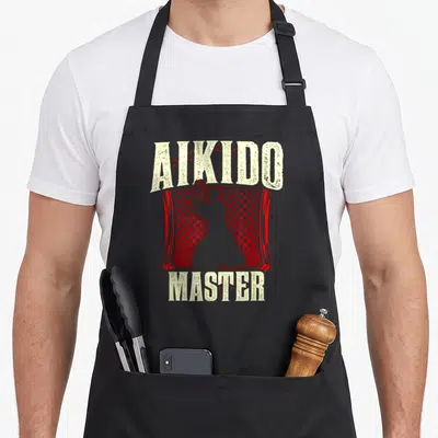 Tablier de cuisine noir avec inscription Aikido Master et silhouette rouge d'un pratiquant d'arts martiaux sur fond de points.