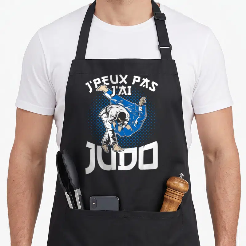 Tablier de cuisine noir avec illustration d'un judoka en action et le texte J'peux pas j'ai judo imprimé en blanc et bleu.