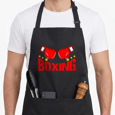 Tablier de cuisine noir avec deux gants de boxe rouges, des étoiles jaunes et le texte BOXING en rouge
