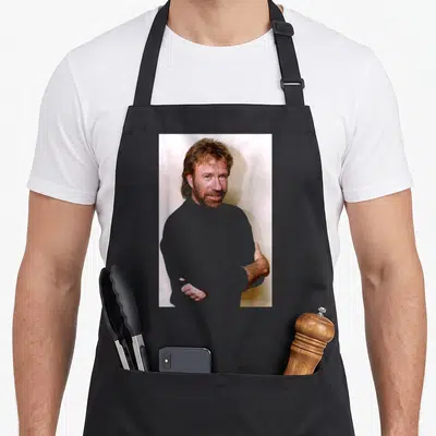Tablier de cuisine noir avec portrait de Chuck Norris bras croisés regard intense