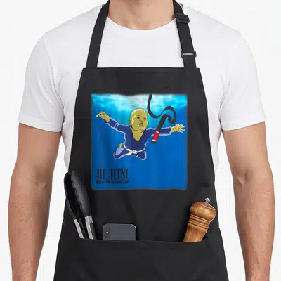 Tablier de cuisine noir avec un bébé en gi bleu plongant vers une ceinture noire BJJ sur fond bleu aquatique.