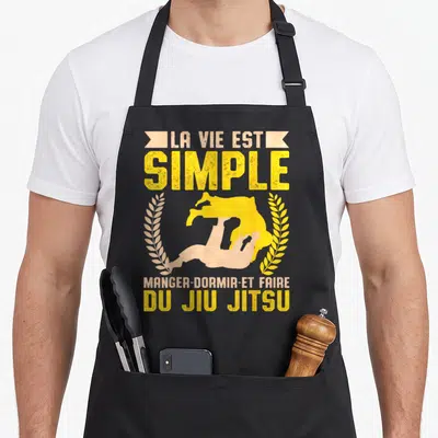 Tablier de cuisine noir avec silhouette jaune de jiu-jitsu et texte La Vie Est Simple Manger Dormir Du Jiu Jitsu encadré de lauriers.