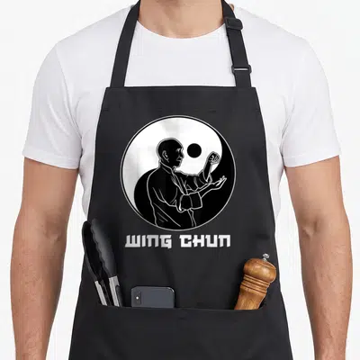 Tablier de cuisine noir avec illustration blanche d'un pratiquant de Wing Chun dans un cercle Yin Yang et le texte WING CHUN en bas.