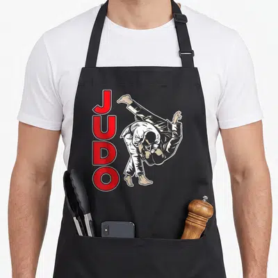 Tablier de cuisine noir avec illustration de judokas et le mot JUDO en lettres rouges verticales.