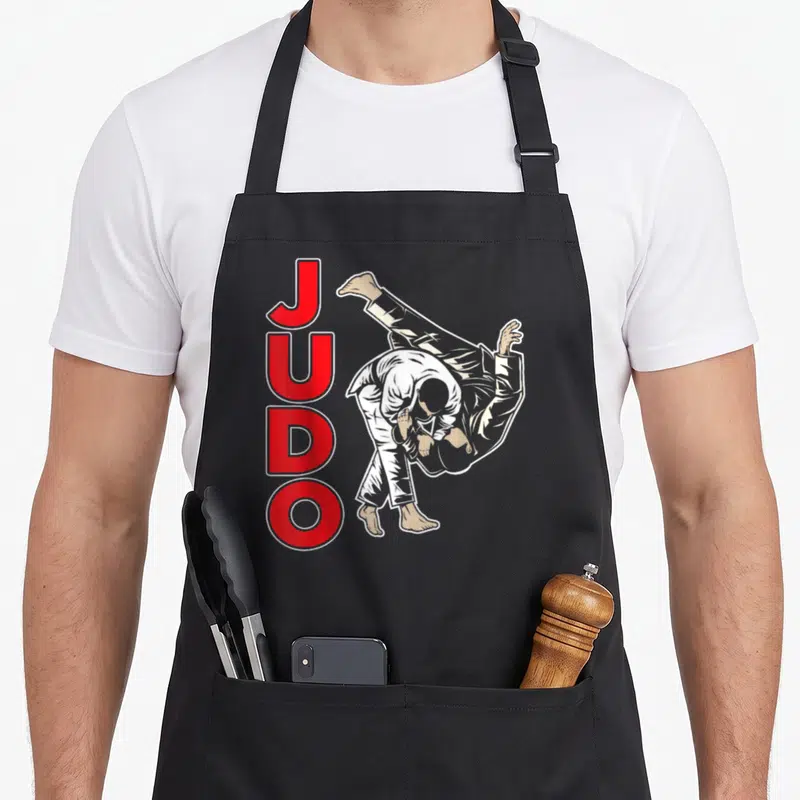 Tablier de cuisine noir avec illustration de judokas et le mot JUDO en lettres rouges verticales.