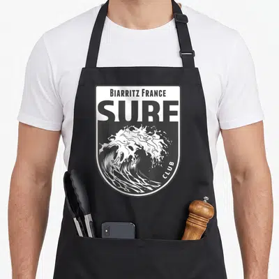 Tablier de cuisine noir avec un insigne blanc représentant une vague et le texte Biarritz France Surf Club.