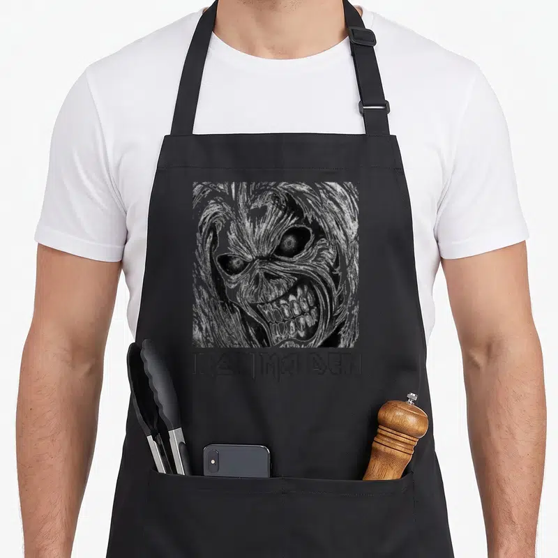 Tablier de cuisine noir avec l'illustration monochrome du personnage Eddie et le logo stylisé Iron Maiden en dessous.