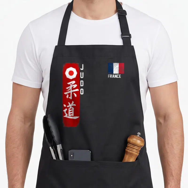 Tablier de cuisine noir avec inscription JUDO, kanji blanc sur bande rouge et petit drapeau France en haut à droite.