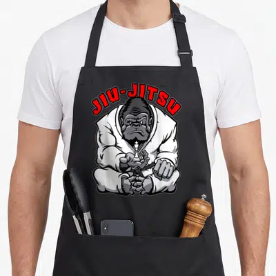 Tablier de cuisine noir avec illustration d'un gorille en kimono blanc tenant une pièce d'échecs et le texte JIU-JITSU en rouge.