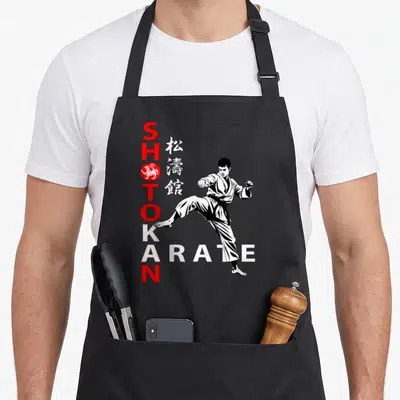 Tablier de cuisine noir avec illustration d'un karatéka effectuant une frappe haute sous le mot Shotokan Karaté vertical.