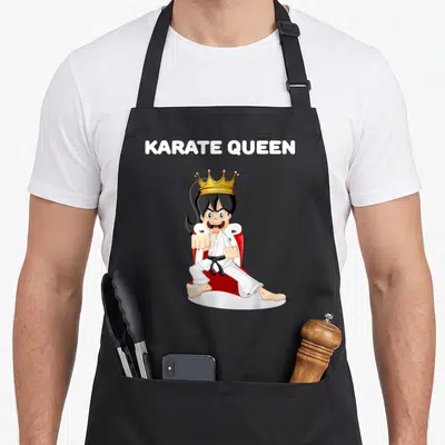 Tablier de cuisine noir avec illustration d'une Karate Queen coiffée d'une couronne dorée en position de combat sur trône rouge.