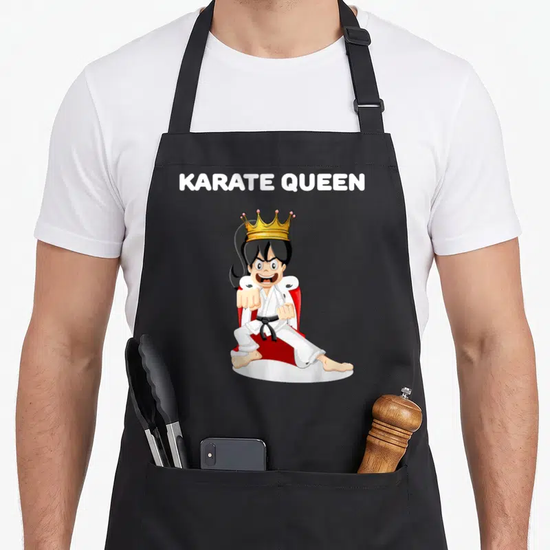 Tablier de cuisine noir avec illustration d'une Karate Queen coiffée d'une couronne dorée en position de combat sur trône rouge.