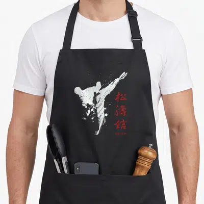 Tablier de cuisine noir avec silhouette de coup de pied blanc et idéogrammes rouges verticaux.