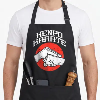 Tablier de cuisine noir avec une poignée de main blanche sur cercle rouge et texte KENPO KARATE en haut.