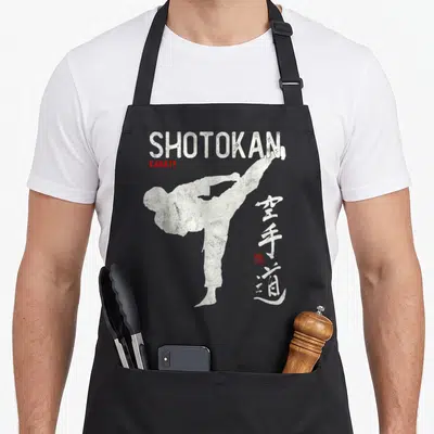 Tablier de cuisine noir avec silhouette blanche de karatéka en haute frappe et texte Shotokan Karate.