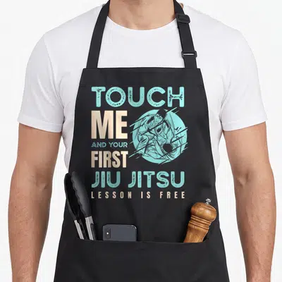 Tablier de cuisine noir avec l'inscription Touch Me First Jiu Jitsu Lesson Is Free et une illustration de grapheur.