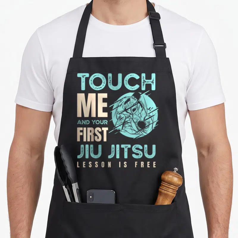 Tablier de cuisine noir avec l'inscription Touch Me First Jiu Jitsu Lesson Is Free et une illustration de grapheur.