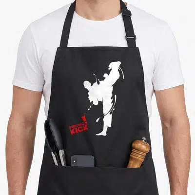 Tablier de cuisine noir avec silhouette blanche effectuant une frappe haute et logo Strong Kick rouge en bas à gauche.