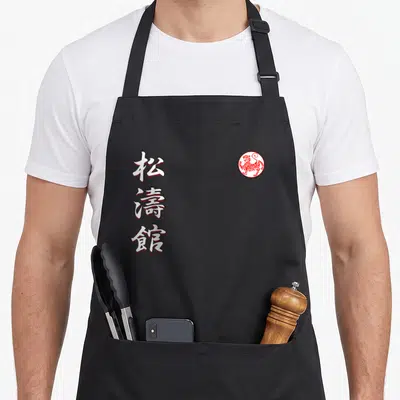 Tablier de cuisine noir avec caractères japonais blancs et sceau circulaire rouge représentant un tigre stylisé.