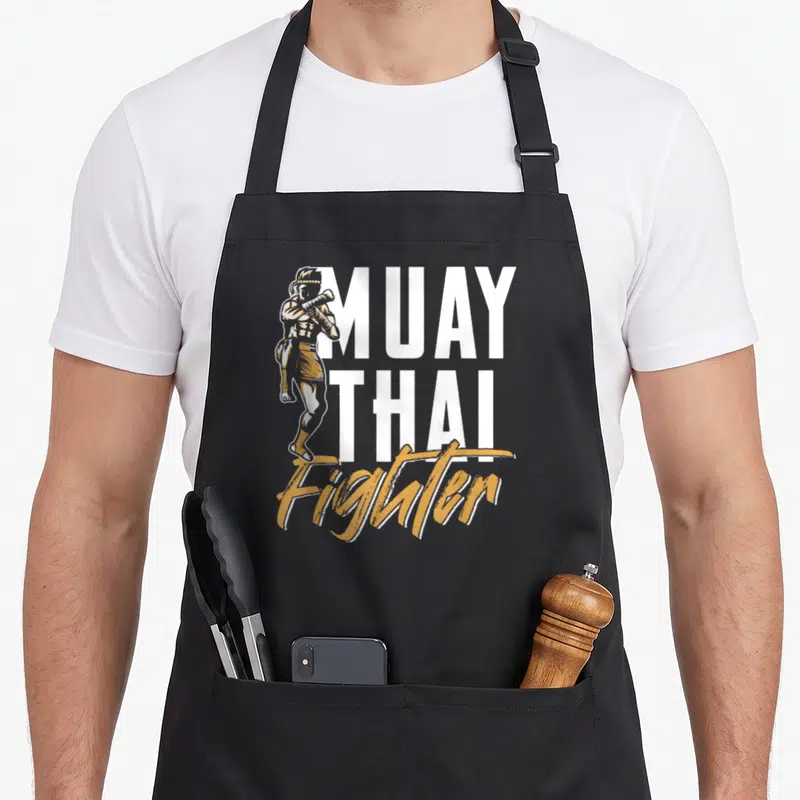 Tablier de cuisine noir avec illustration d'un boxeur et texte Muay Thai Fighter en blanc et orange.
